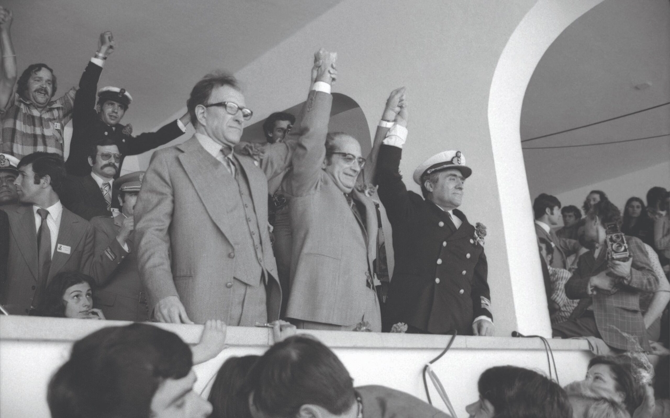 O Presidente da República Costa Gomes, o Primeiro-Ministro Vasco Gonçalves e o Chefe do Estado-Maior da Armada Pinheiro de Azevedo na tribuna das celebrações do 1.º de Maio. Mário Soares, líder do partido vencedor das eleições, foi impedido de aceder à tribuna do Estádio Primeiro de Maio. Lisboa, 01 de maio de 1975. Fotografia de Novo Ribeiro. ANTT, Fundo do jornal «O Século».